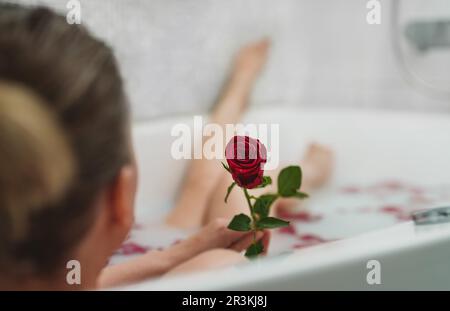 Une femme se détend dans un bain avec du lait et des pétales de rose. Banque D'Images
