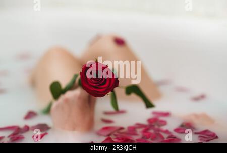Une femme se détend dans un bain avec du lait et des pétales de rose. Banque D'Images
