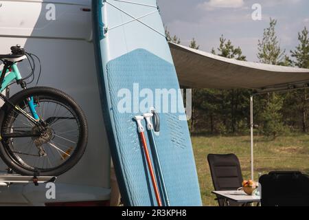 Les planches d'aviron gonflables Sup se tiennent près du camping-car gonflé dans la nature pendant la journée. Banque D'Images