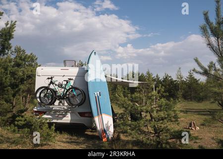 Les planches d'aviron gonflables Sup se tiennent près du camping-car gonflé dans la nature pendant la journée. Banque D'Images