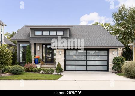Une maison de banlieue de deux étages avec un parement en pierre, une porte de garage moderne avec verre dépoli et un bel aménagement paysager. Banque D'Images