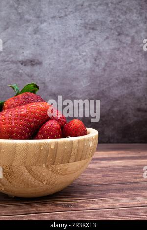 Fraises rouges sucrées fraîchement lavées dans un bol en bois placé sur une table. Image verticale avec mise au point sélective, gouttes d'eau comme un détail. Banque D'Images