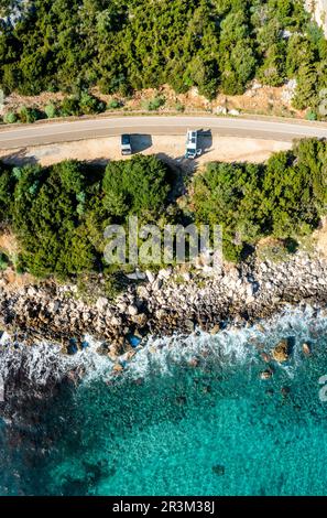 Vue de haut en bas de deux camping-cars stationnés sur une étroite route côtière dans la forêt avec des eaux turquoise et des côtes rocheuses Banque D'Images