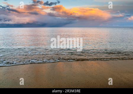 Vagues douces sur la plage de sable doré avec l'océan et le coucher de soleil coloré ciel derrière Banque D'Images