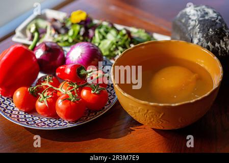 Un gros œuf d'autruche cru dans un bol à côté des légumes et de la salade sur la table. Ingrédients pour cuisiner un plat, shakshuka, omelette. Mise au point sélective douce Banque D'Images