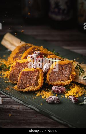 Côtes de bœuf fumées avec os et sauce barbecue sur une assiette carrée blanche, vue de dessus, fond noir rustique. Côtes de bœuf grillées aux os, côtes de bœuf croustillantes Banque D'Images