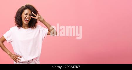 Je n'ai pas peur de m'exprimer. Joyeuse femme afro-américaine charismatique en t-shirt avec coupe de cheveux afro montrant la langue jouée et d Banque D'Images