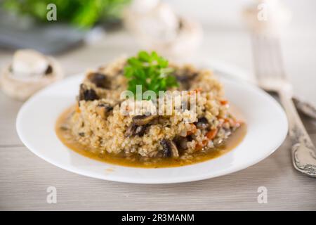 boulgour cuit avec des champignons, des carottes et des légumes dans une assiette, sur une table en bois. Banque D'Images