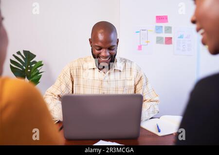 Le développeur noir masculin travaille sur un ordinateur portable lors d'une réunion avec des collègues Banque D'Images