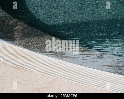 Vue sur la piscine ronde avec de l'eau claire bleue et des reflets d'ondes ombrées de lumière du soleil. Un concept de vacances minimal Banque D'Images