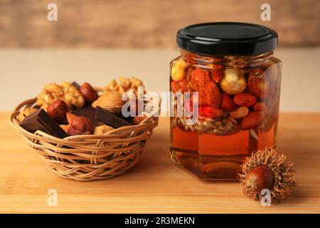 Différents fruits à coque au miel en pot et panier en osier avec en-cas sur une table en bois Banque D'Images