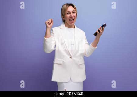 joyeuse jeune femme blondie caucasienne dans une élégante veste tenant smartphone avec maquette Banque D'Images