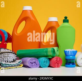 Bouteilles en plastique orange avec produits liquides et sacs à ordures sur une table blanche, fond jaune Banque D'Images