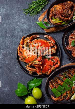 Ensemble de plats de fruits de mer. Crabes, poulpes, calmars et crevettes tigrées sur des casseroles en fonte et des assiettes sur fond noir. Vue de dessus. Co Banque D'Images