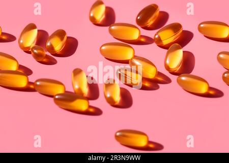 Composition de pilules de vitamine orange dispersées sur fond rose en studio léger Banque D'Images