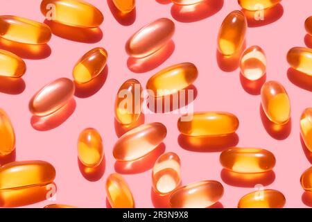 Composition de pilules de vitamine orange dispersées sur fond rose en studio léger Banque D'Images