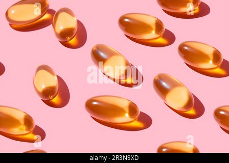 Composition de pilules de vitamine orange dispersées sur fond rose en studio léger Banque D'Images