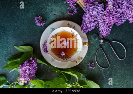 Vue de dessus de savoureux thé noir dans une tasse de blanc vintage sur table en béton vert menthe avec des fleurs de lilas aromatiques Banque D'Images