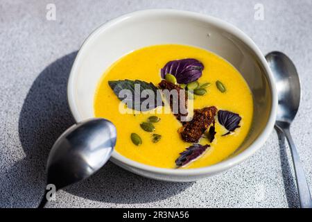 Bol en céramique grand angle avec soupe à la crème de potiron aux herbes de basilic, pain de seigle et graines sur fond flou Banque D'Images