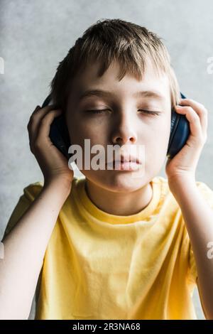 Portrait des yeux sérieux, ferme un garçon aux cheveux bruns, portant un t-shirt jaune et touchant un casque tout en écoutant de la musique sur un arrière-plan flou Banque D'Images