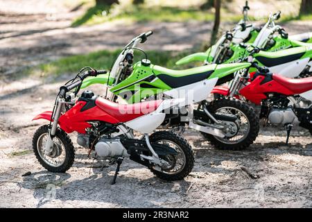 Une rangée de petites motos colorées pour les enfants garés au sol à l'ombre à louer dans un parc ensoleillé Banque D'Images