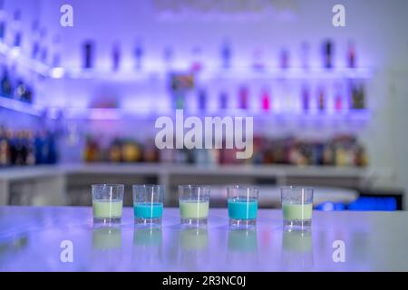 Rangée de doses servies avec des liqueurs bleues et blanches placées en rangée sur le comptoir contre des étagères floues avec des bouteilles dans le bar du restaurant Banque D'Images