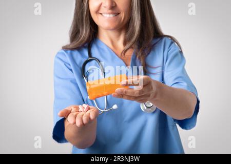 Gaie médecin femme versant des pilules de pot sur la main, se tenant isolé sur fond gris, gros plan, rogné Banque D'Images