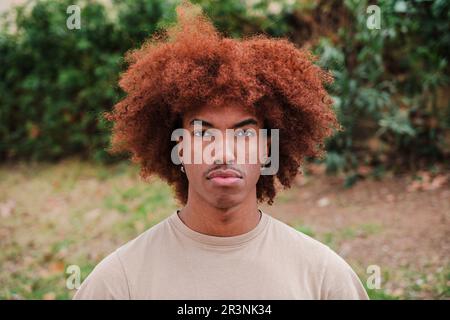 Jeune afro-américain regardant sérieusement la caméra. Gros plan de l'adolescent de sexe masculin avec une attitude pensive. vue de face d'un homme attentionné avec des cheveux afro debout à l'extérieur. Vrai jeune masculin. Photo de haute qualité Banque D'Images