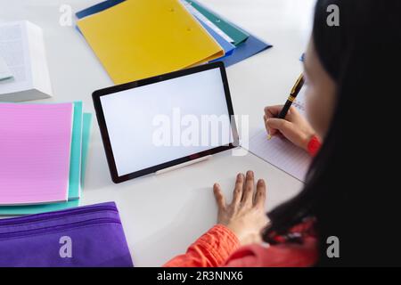 Image d'une femme biraciale utilisant une tablette avec un espace de copie à l'écran assis au bureau Banque D'Images