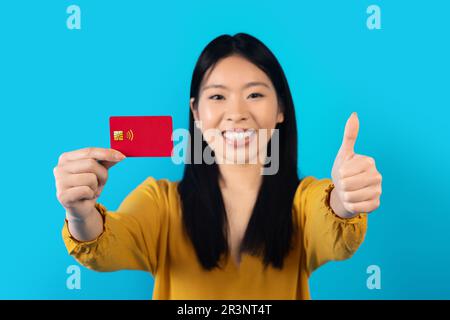 Jeune femme chinoise joyeuse montrant une carte bancaire bleue Banque D'Images