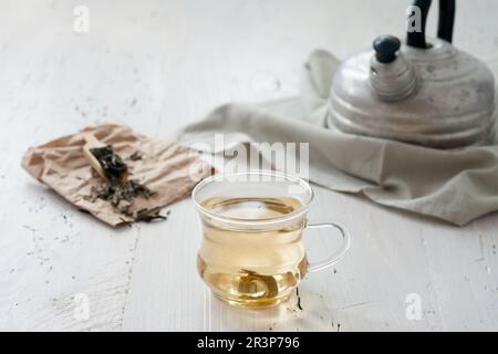 Thé blanc fraîchement préparé sur une planche de bois abîmée avec théière vintage en arrière-plan Banque D'Images