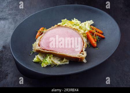 Steak de porc Kasseler en croûte de pâte avec chou de savoie et carottes servi en gros plan sur une assiette design Banque D'Images