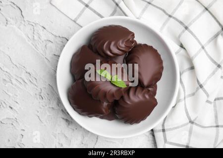 Délicieux zèphans enrobés de chocolat avec menthe dans un bol sur fond gris clair, vue de dessus Banque D'Images