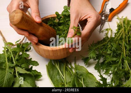 Femme moulant des herbes vertes fraîches dans le mortier à la table en bois blanc, gros plan Banque D'Images