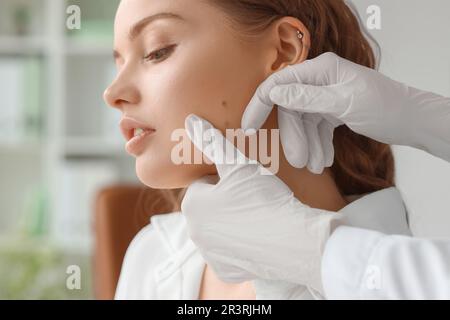 Dermatologue examinant les grains de beauté sur le visage de la jeune femme en clinique, en gros plan Banque D'Images