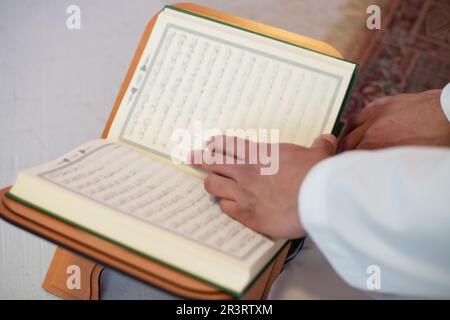 Jeune homme musulman arabe en vêtements traditionnels lisant le livre Saint Coran sur le tapis de prière avant un dîner iftar pendant un ramad Banque D'Images