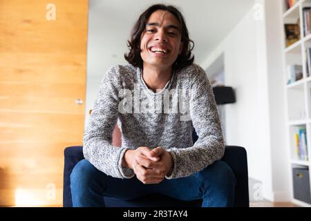 Heureux biracial homme assis sur le canapé, ayant l'appel vidéo et souriant Banque D'Images