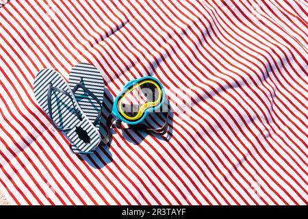 Vue en grand angle des tongs bleues avec des lunettes de natation sur la serviette de plage pendant la journée ensoleillée Banque D'Images