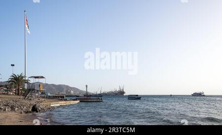 Coucher de soleil sur la plage d'Aqaba, fenêtre de la Jordanie sur la mer Rouge. En arrière-plan, l'impressionnant Flagpole et les installations portuaires Banque D'Images