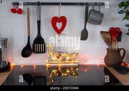 L'intérieur de la cuisine de la maison est décoré de coeurs rouges pour la Saint-Valentin. Décoration sur la table, cuisinière, ustensiles, Banque D'Images