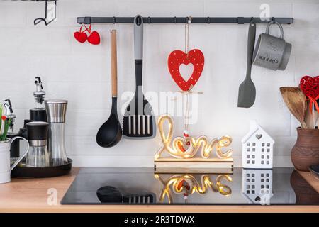 L'intérieur de la cuisine de la maison est décoré de coeurs rouges pour la Saint-Valentin. Décoration sur la table, cuisinière, ustensiles, Banque D'Images