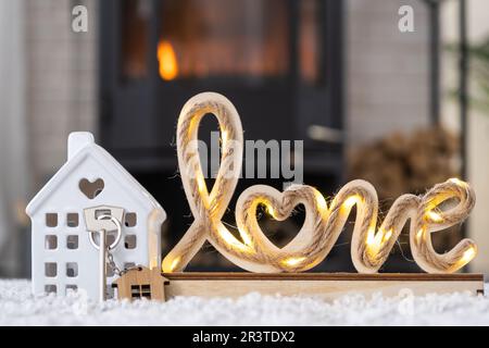 Clé à la maison avec porte-clés contre le fond de la cheminée poêle avec feu et bois de chauffage dans le décor de la Saint-Valentin, l'amour maison. Déplacement vers Banque D'Images