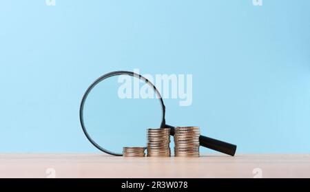 Une pile de pièces de monnaie en métal et une loupe en plastique sur fond bleu. Le concept de l'augmentation des impôts, des subventions Banque D'Images