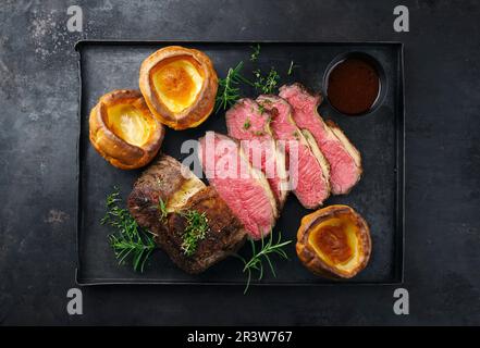 Rôti de bœuf traditionnel du Commonwealth dimanche coupé en tranches avec du Yorkshire pudding et une sauce au vin rouge servi en vue sur un noir rustique Banque D'Images