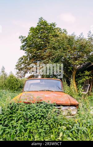 Abandonné voiture soviétique rouillée sur cour rurale avec des bâtiments en bois Banque D'Images