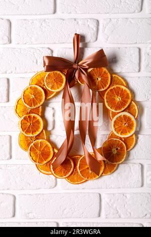 Couronne décorative faite d'oranges sèches et de ruban accroché au mur de briques blanches Banque D'Images