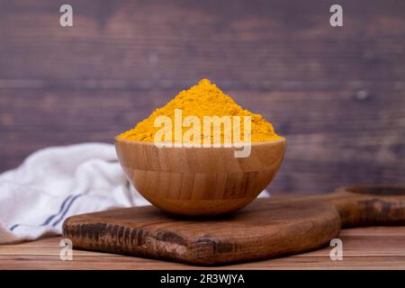 Curcuma en poudre sur fond en bois. Épices en poudre de curcuma moulues séchées dans un bol en bois Banque D'Images