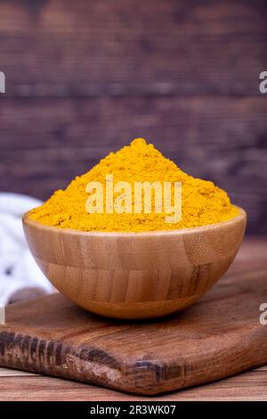 Curcuma en poudre sur fond en bois. Épices en poudre de curcuma moulues séchées dans un bol en bois. Gros plan Banque D'Images