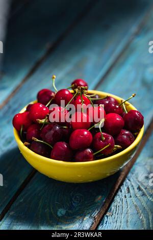 Un seul bol jaune de cerises fraîches sur bois bleu dans une lumière spectaculaire. scène minimale Banque D'Images