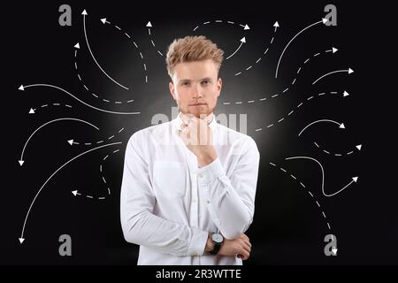 Choix dans la profession ou dans d'autres domaines de la vie, concept. Prenant la décision, un jeune homme attentif entouré de flèches dessinées sur fond noir Banque D'Images